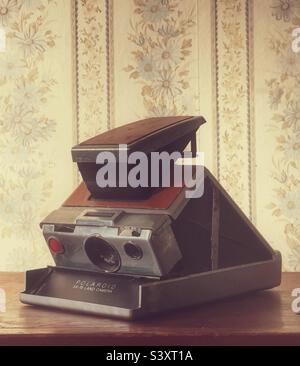 Fotocamera Polaroid SX-70 d'epoca seduta su uno scaffale in legno con sfondo vintage floreale Foto Stock