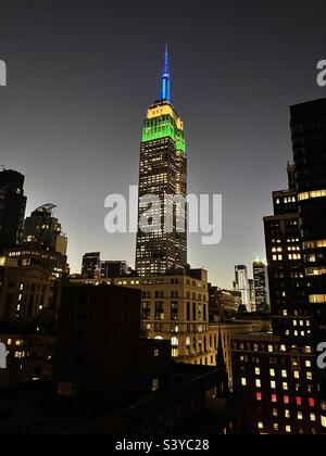 Le luci della torre dell'Empire state Building si illuminano di giallo verde e blu contro un cielo serale a New York City, USA Foto Stock