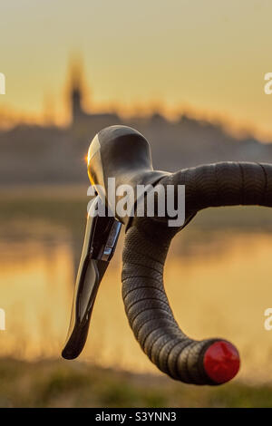 Un manubrio rosso nero per bicicletta da corsa con freni si sposta contro la silhouette di uno skyline della città di Dresda nella luce della sera Foto Stock