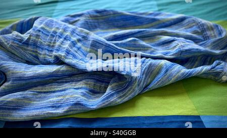 Camicia in lino rumpled blu, verde e indaco su copriletto blu, verde e indaco, creando un'immagine astratta, adatta per lo sfondo grafico Foto Stock