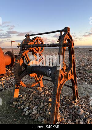 Verricello arrugginito sulla spiaggia di ciottoli al tramonto/ora d'oro. Foto Stock