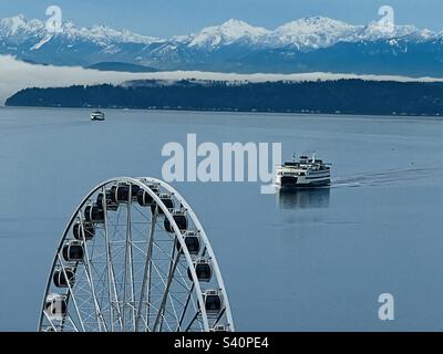 Traghetti che viaggiano attraverso il Mare di Salish in Elliot Bay a Seattle, USA con le montagne olimpiche piene di neve che si esibiscono all'alba. Foto Stock