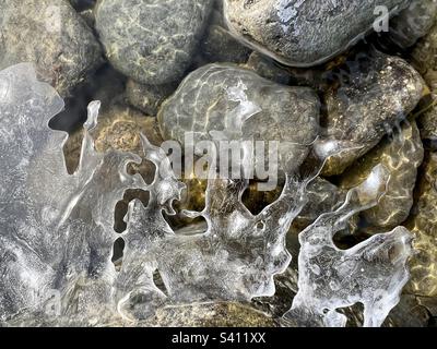 Sculture di ghiaccio filigrana in un fiume con il sole che si riflette sulle rocce sottostanti. Le formazioni di ghiaccio dimostrano splendidamente l’eleganza della natura. Foto Stock