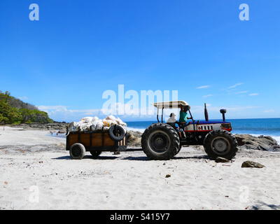 Un trattore prende sacchi di rifiuti lungo la spiaggia per il riciclaggio in Costa Rica Foto Stock