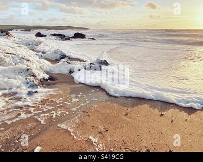 Mare schiumoso con alta marea al largo della costa di Broad Beach, traeth llydan, Rhosneigr, Anglesey, Galles del Nord Foto Stock