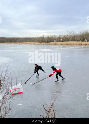 Due ragazzi giocano a hockey su ghiaccio in un laghetto ghiacciato nel New Jersey, USA. Foto Stock