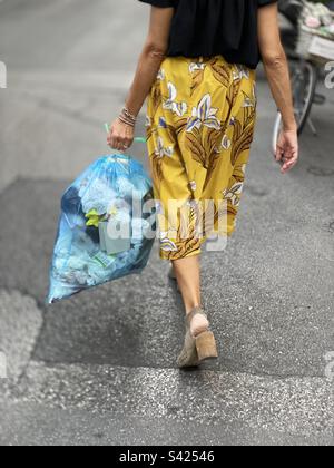 Donna da dietro a camminare prendendo la spazzatura fuori in sacchetto di plastica Foto Stock