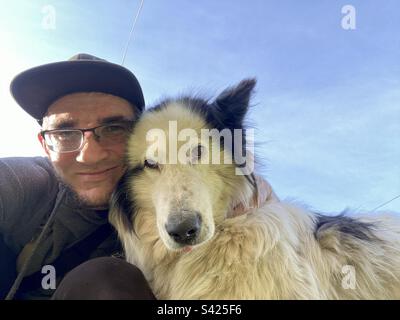 Un uomo sorridente con occhiali abbraccia un cane bianco di un amico della razza Yakut Laika. Foto Stock