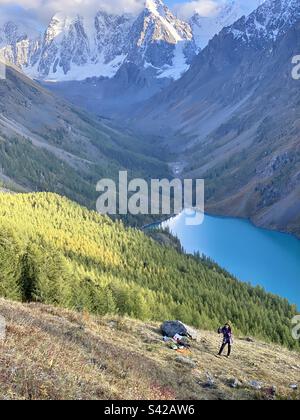 Una ragazza asiatica Yakut sorride su una collina sopra un lago alpino e montagne con ghiacciai e neve nell'Altai. Foto Stock