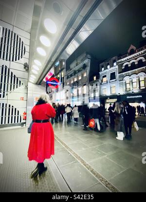 Una donna con un cappotto rosso esce dalla stazione della metropolitana di Londra Foto Stock