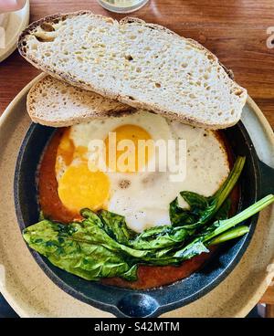 Fuoco uova arrosto con verdi su un letto di fagioli con pane tostato con pasta madre. Foto Stock