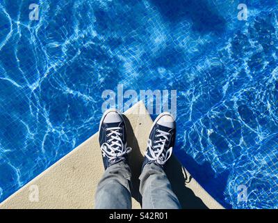 Guardando giù sui piedi che indossano le sneakers al bordo di una piscina Foto Stock