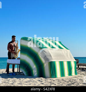 Gennaio 2023, Busker suona un sassofono di fronte a un cabana spiaggia, South Beach, Miami Beach, Florida, Stati Uniti Foto Stock