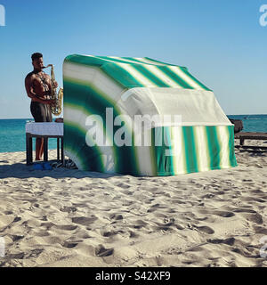 Gennaio 2023, Busker suona un sassofono di fronte a un cabana spiaggia, South Beach, Miami Beach, Florida, Stati Uniti Foto Stock