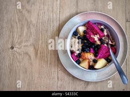 Direttamente sopra il colpo di farina d'avena con frutta fresca e mirtilli secchi in una ciotola con cucchiaio su piatto su tavolo di legno. Foto Stock