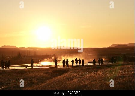 Un piccolo gruppo di turisti si riunisce al tramonto per guardare e aspettare un'eruzione geyser in Islanda Foto Stock