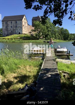 Una ragazza corre a un motoscafo presso un molo vicino al bellissimo castello antico di Kastelholm, nell'arcipelago delle isole Åland, nella regione del Mar Baltico in Finlandia, in estate. Foto Stock
