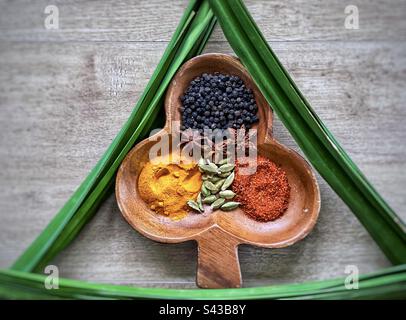 Direttamente sopra la vista di spezie colorate disposte in un contenitore decorativo di legno incorniciato da foglie di pandano anche noto come pandan o foglie di pino a vite su legno. Foto Stock