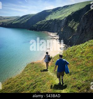 Due turisti scendono verso una romantica spiaggia segreta sotto una scogliera su una spettacolare sezione del popolare percorso della Costa di Ceredigion vicino a Llangrannog nel Galles Occidentale Foto Stock