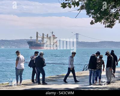 Un gruppo di giovani pesci sulle rive del Bosforo mentre una nave enorme naviga oltre Foto Stock