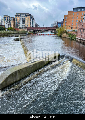Fiume che scorre attraverso Leeds con ponte weir braccio arancione e flusso eccessivo Foto Stock