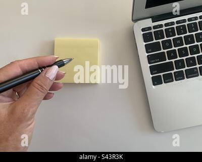 Donna con una penna in mano che prende appunti accanto al suo computer portatile Foto Stock