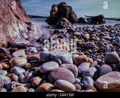 Ghiaia su una spiaggia, con lunga esposizione di marea che entra. Foto Stock