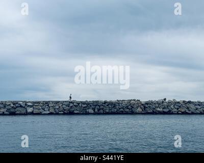 Lone figura a piedi lungo un frangiflutti su una nuvolosa da Foto Stock