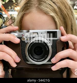 Giovane ragazza di 10 anni che impara nuove abilità scattando una foto con una vecchia macchina fotografica di stile un modello originale fujifilm x100 Foto Stock