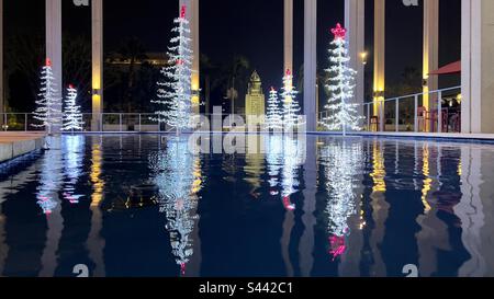 LOS ANGELES, CA, DEC 2022: Alberi di Natale a vista ampia decorati con LED bianchi e rossi, con riflessi in acqua al Music Center in Downtown. Municipio sullo sfondo, illuminato di notte Foto Stock