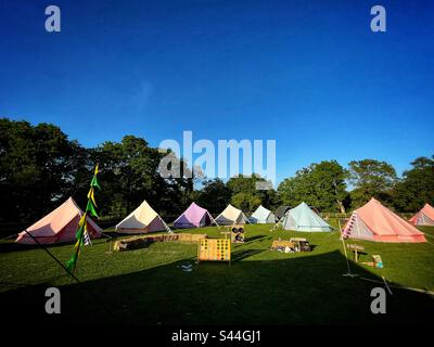 Tende campanaria multicolore sono viste in un campo rurale davanti a un mini festival in Hampshire, Inghilterra. Foto Stock