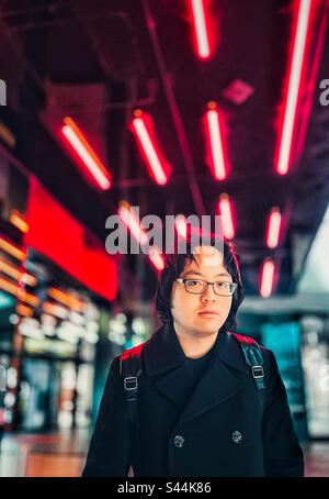 Ritratto di giovane asiatico in occhiali che si contrappongono a luci al neon multicolore nella città di notte. Foto Stock