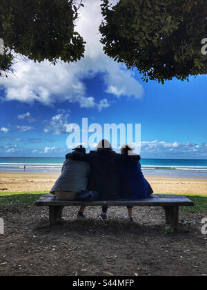 Tre persone sedettero su una panchina a Lorne Beach Victoria Australia Foto Stock