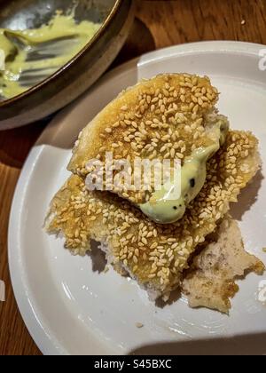 Primo piano di focaccia al sesamo parzialmente consumata con crema di avocado sul piatto sul tavolo. Foto Stock