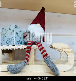 Babbo Natale, giocattolo felpato nella cabina natalizia dell'aeroporto di Helsinki, seduto su una slitta di legno con un regalo confezionato Foto Stock