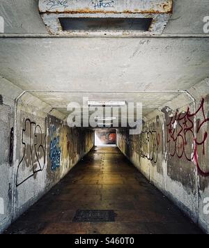 Una metropolitana sotterranea sembra poco invitante - buia, umida e malandata. Le pareti spruzzate con graffiti si trovano su entrambi i lati del passaggio. Foto Stock