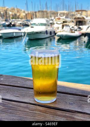 Bicchiere di birra fredda su un tavolo in un bar affacciato sulle barche in un porticciolo in tre città a la Valletta, Malta Foto Stock