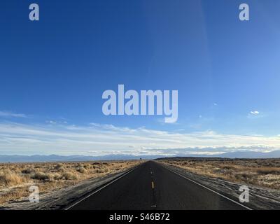 Punto panoramico alto con asfalto nero basso nel telaio, con marcature gialle luminose sull'autostrada attraverso il deserto nella California meridionale. Cielo blu sopra la testa Foto Stock