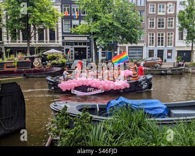 Una barca galleggiante su un canale d'acqua olandese ad Amsterdam con una folla di persone che celebrano Pride 2022 Foto Stock