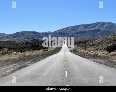 Ammira la strada che attraversa il deserto e le colline pedemontane, verso le montagne della California meridionale. Cielo blu sopra la testa, pali del telegrafo sul lato della strada Foto Stock