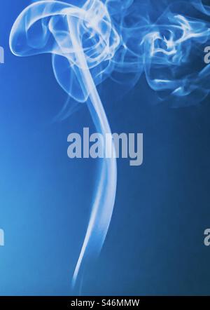 Smoke swirling from an incense stick against blue background Stock Photo