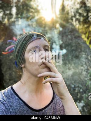 Donna che fuma un grosso spinello al tramonto Foto Stock