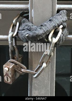 Big gray padlock that closes an iron gate with a ring chain. Grosso lucchetto grigio che chiude con una catena ad anelli un cancello di ferro. Foto Stock