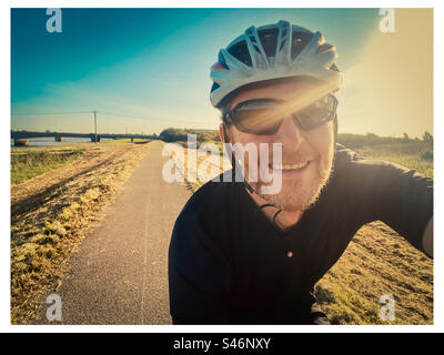 Un ciclista felice cavalca al sole lungo una pista ciclabile pianeggiante vicino a Kings Lynn a Norfolk Foto Stock