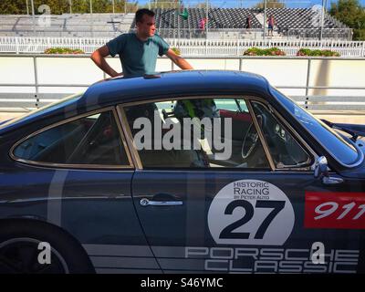 Pilota da corsa seduto in una Porsche 911 grigia degli anni '1960 nella pit Lane del circuito automobilistico di Goodwood nel Regno Unito Foto Stock