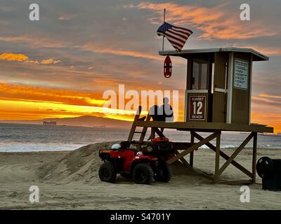 Bagnino alla torre 12 di Sunset Beach (Huntington Beach, California), guardando l'acqua verso la penisola di Palos Verdes mentre il sole tramonta. Foto Stock