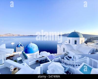 Le chiese bianche con cupole blu annidate sulle pendici della caldera di Oia, Santorini, poco prima del tramonto Foto Stock