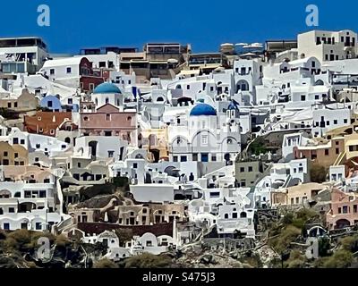 Tra i numerosi edifici bianchi che costeggiano il pavimento della caldera di Oia, Santorini, spiccano chiese con cupola blu. Foto Stock