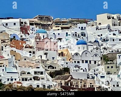 Cupole e strutture di chiese blu colorate in mezzo a molti edifici bianchi che si trovano sopra la caldera dell'isola di Santorini a Oia. Foto Stock