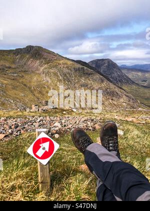 Escursionista che fa una pausa sul sentiero prima della discesa finale da una montagna scozzese Foto Stock